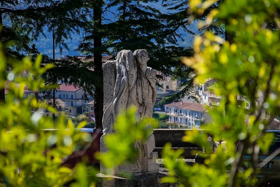 Dettaglio di un monumento Tommaso Campanella in pietra immerso nel verde con vista panoramica sul borgo di Altomonte sullo sfondo